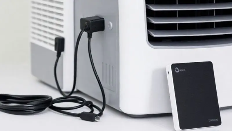 Close-up de um ar-condicionado portátil ao lado de suas fontes de alimentação: um adaptador 12V, um cabo USB e uma bateria externa.
